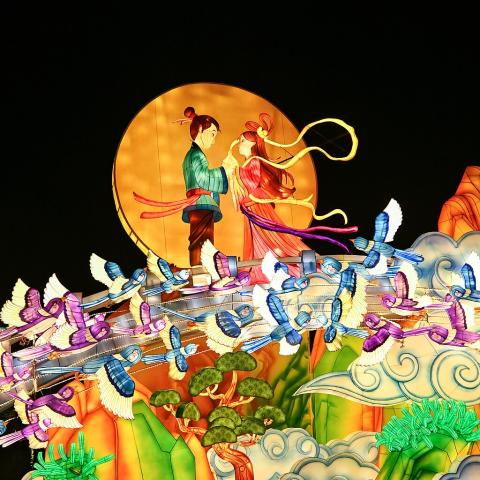 An artwork of a man and women standing holding hands with the sun behind them. They stand on a bridge made of colourful magpies in flight.