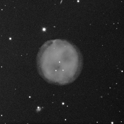 A spherical nebula against a black background with some small white dots of stars. The nebula is cloud-like, grey, and fuzzy.