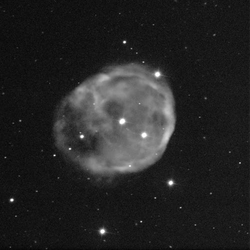 A spherical nebula against a black background with some small white dots of stars. The nebula is cloud-like, grey, and fuzzy.