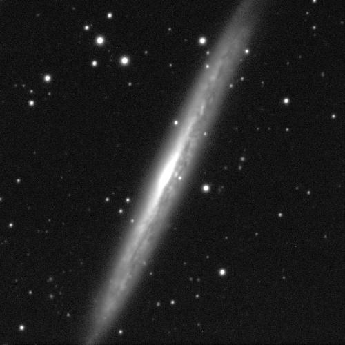 A black and white image of a side-on galaxy. It looks like a thick diagonal line with a bright white glow in the middle.