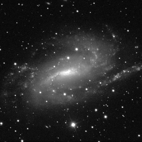 A spiral galaxy against a black background with some small dots of stars. The centre of the galaxy, in the middle of the image, appears almost like a thick, white, vertical line. Spiral arms extend away towards the left and the right, with fuzzy grey around the galaxy's centre and spiral arms.